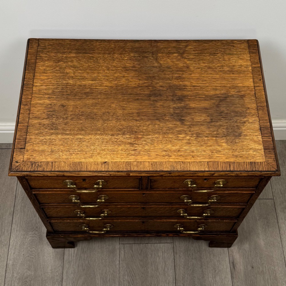 An antique oak chest of drawers featuring two short over three long drawers with brass swan-neck handles and shaped bracket feet. View IX