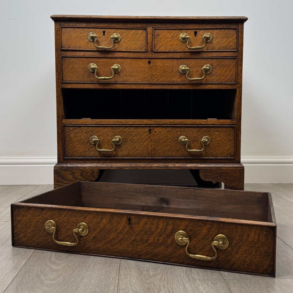 An antique oak chest of drawers featuring two short over three long drawers with brass swan-neck handles and shaped bracket feet. View X