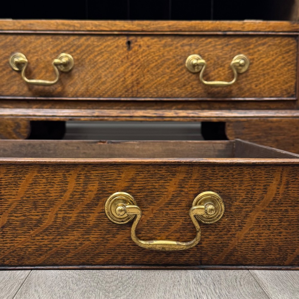 An antique oak chest of drawers featuring two short over three long drawers with brass swan-neck handles and shaped bracket feet. View XI