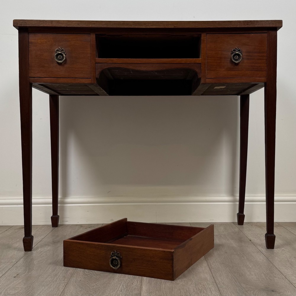 An early 20th-century mahogany writing table featuring three drawers with decorative brass ring handles and square tapered legs. View X