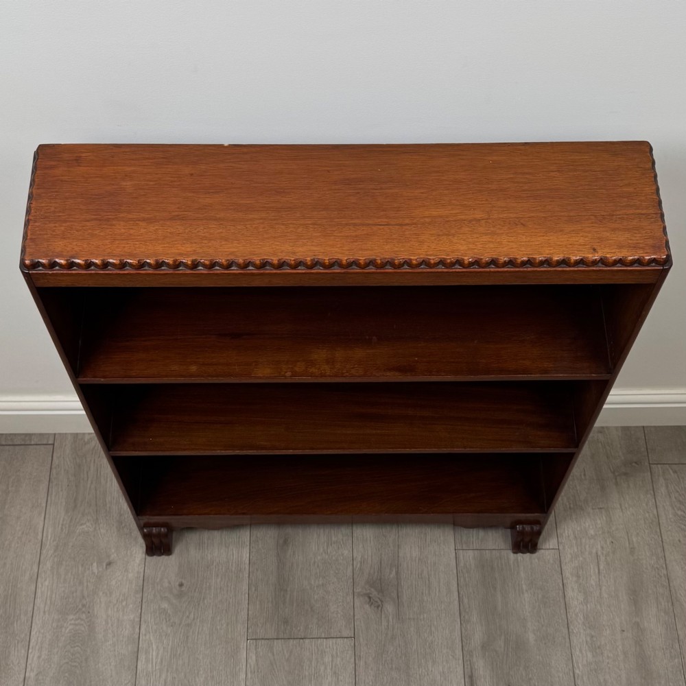 An antique narrow mahogany open bookcase featuring three tiers, a gadrooned top edge, and carved bracket feet. View X