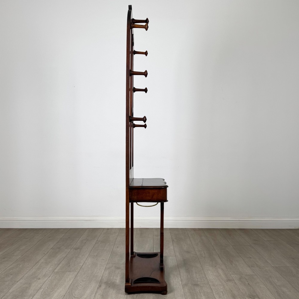 A freestanding Victorian mahogany hall stand featuring turned coat pegs, a narrow central mirror panel, a small shelf, and an umbrella holder base. View VII