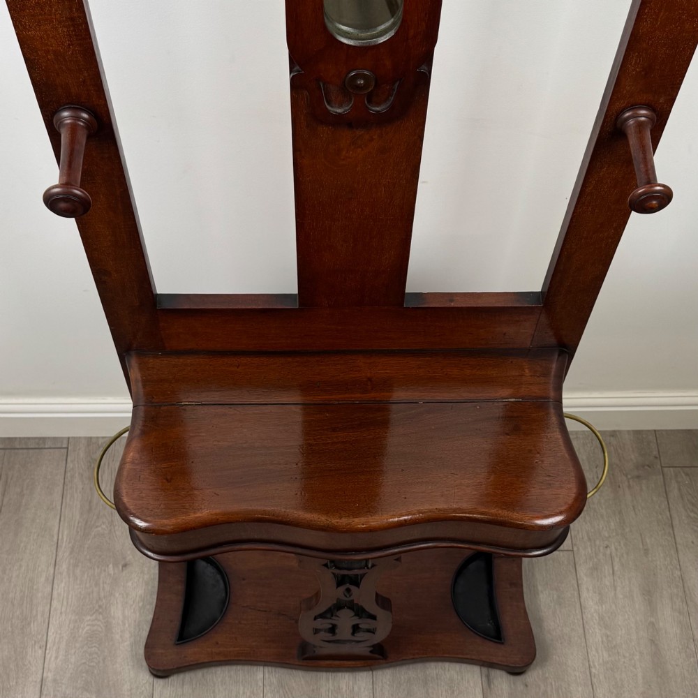 A freestanding Victorian mahogany hall stand featuring turned coat pegs, a narrow central mirror panel, a small shelf, and an umbrella holder base. View IX