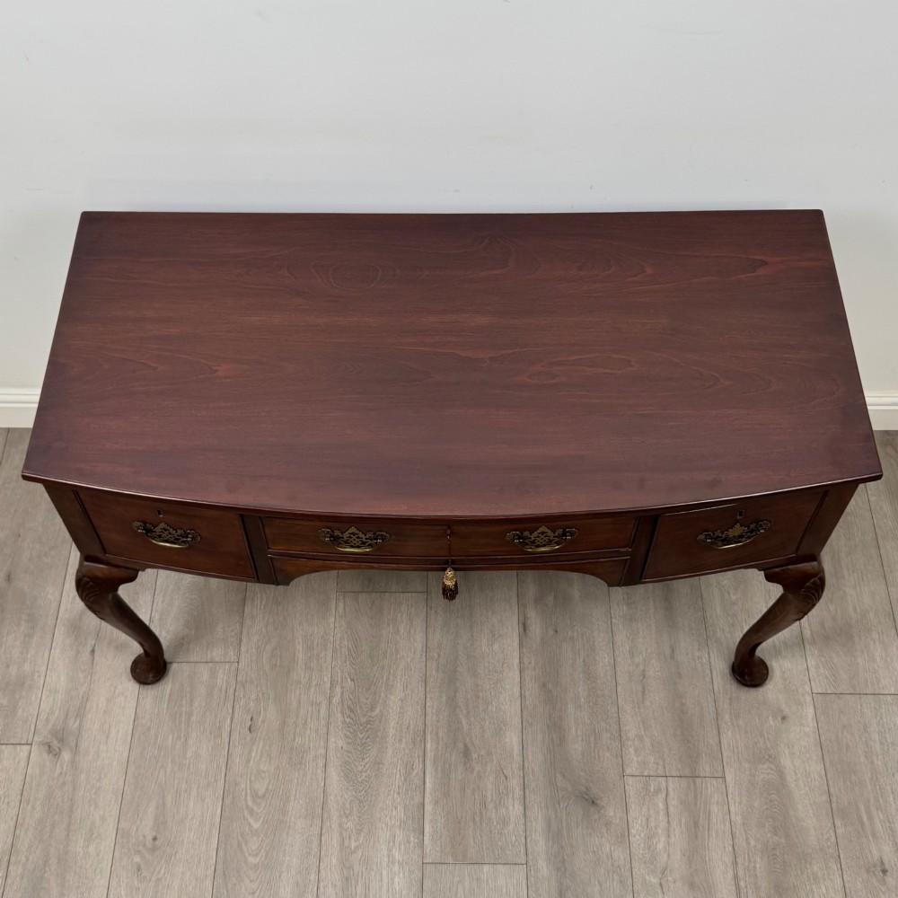 An Edwardian mahogany writing table with cabriole legs, carved knee detailing, three drawers with ornate brass handles, and a central arched kneehole. View IX
