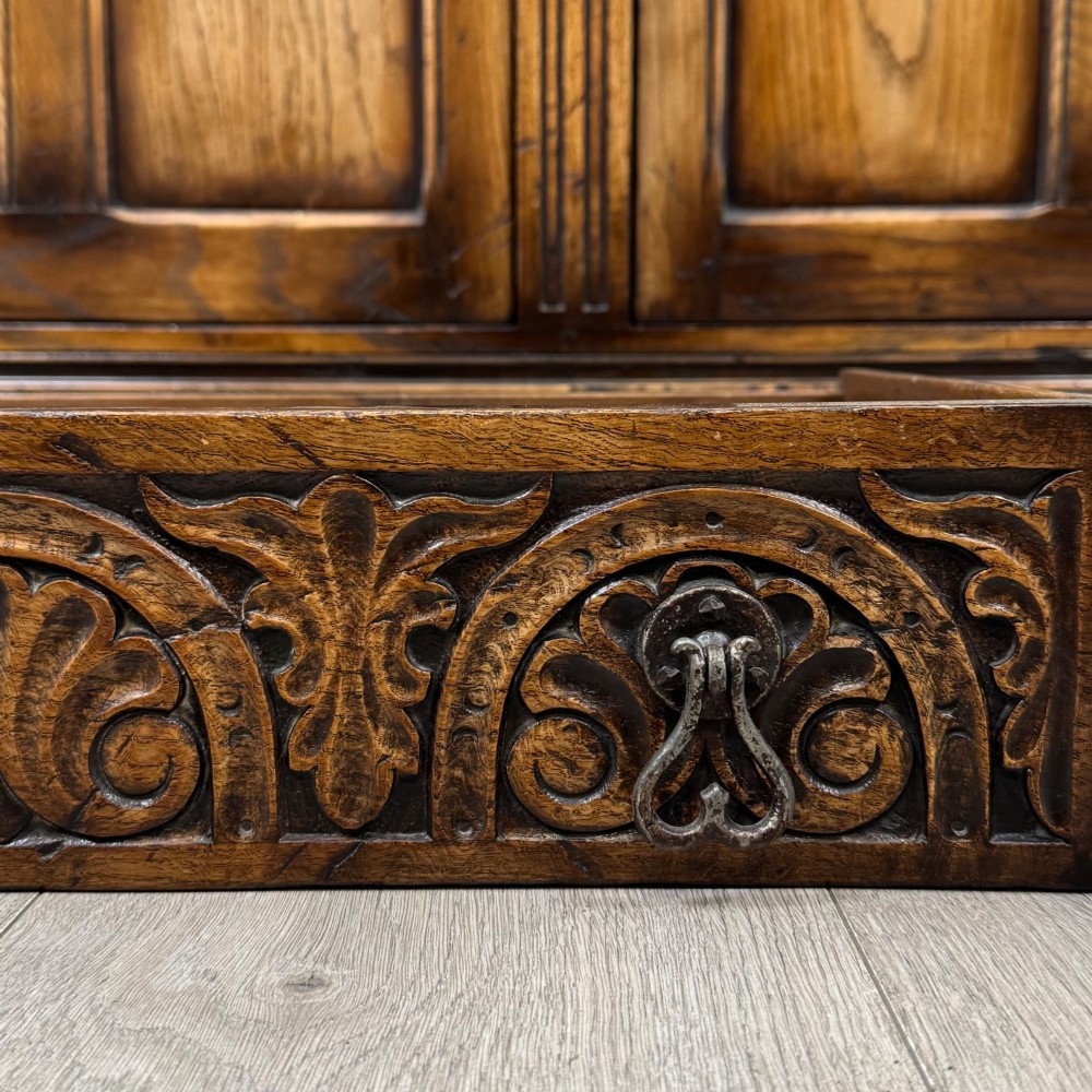 A dark carved oak court cupboard featuring two top doors with relief carving, bulbous turned supports, two drawers, and two panelled cupboard doors below. View XII