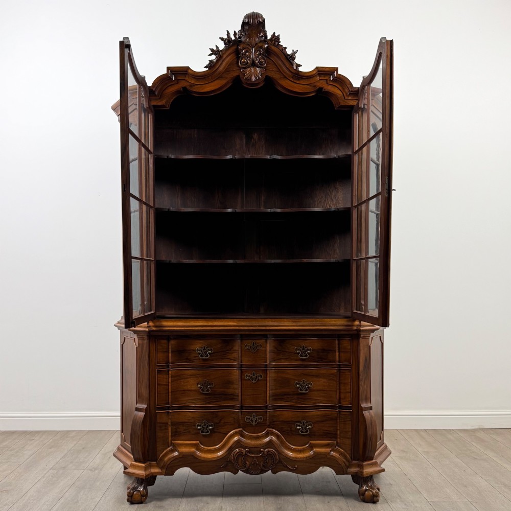 A Dutch walnut display cabinet featuring a carved bonnet-top pediment, multi-pane glazed doors, and a lower chest of drawers on carved claw-and-ball feet. View II