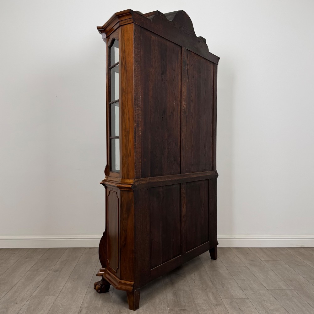 A Dutch walnut display cabinet featuring a carved bonnet-top pediment, multi-pane glazed doors, and a lower chest of drawers on carved claw-and-ball feet. View V