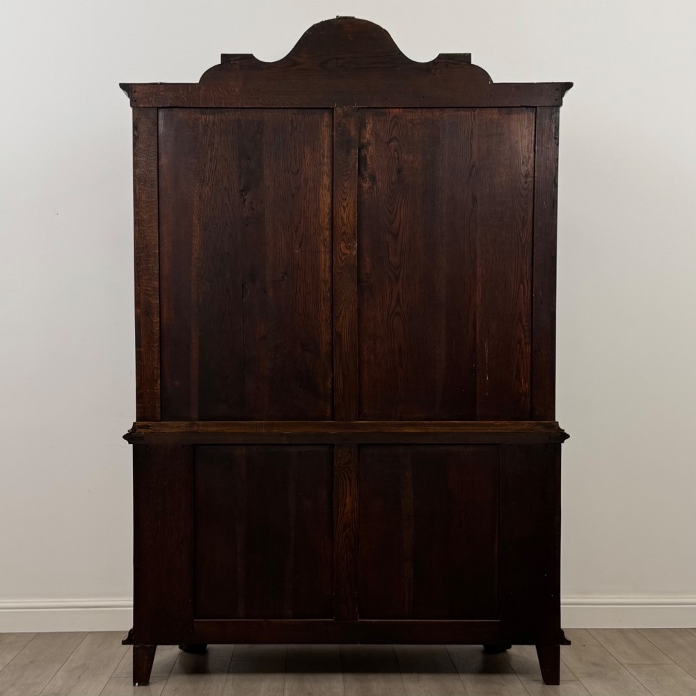 A Dutch walnut display cabinet featuring a carved bonnet-top pediment, multi-pane glazed doors, and a lower chest of drawers on carved claw-and-ball feet. View VI