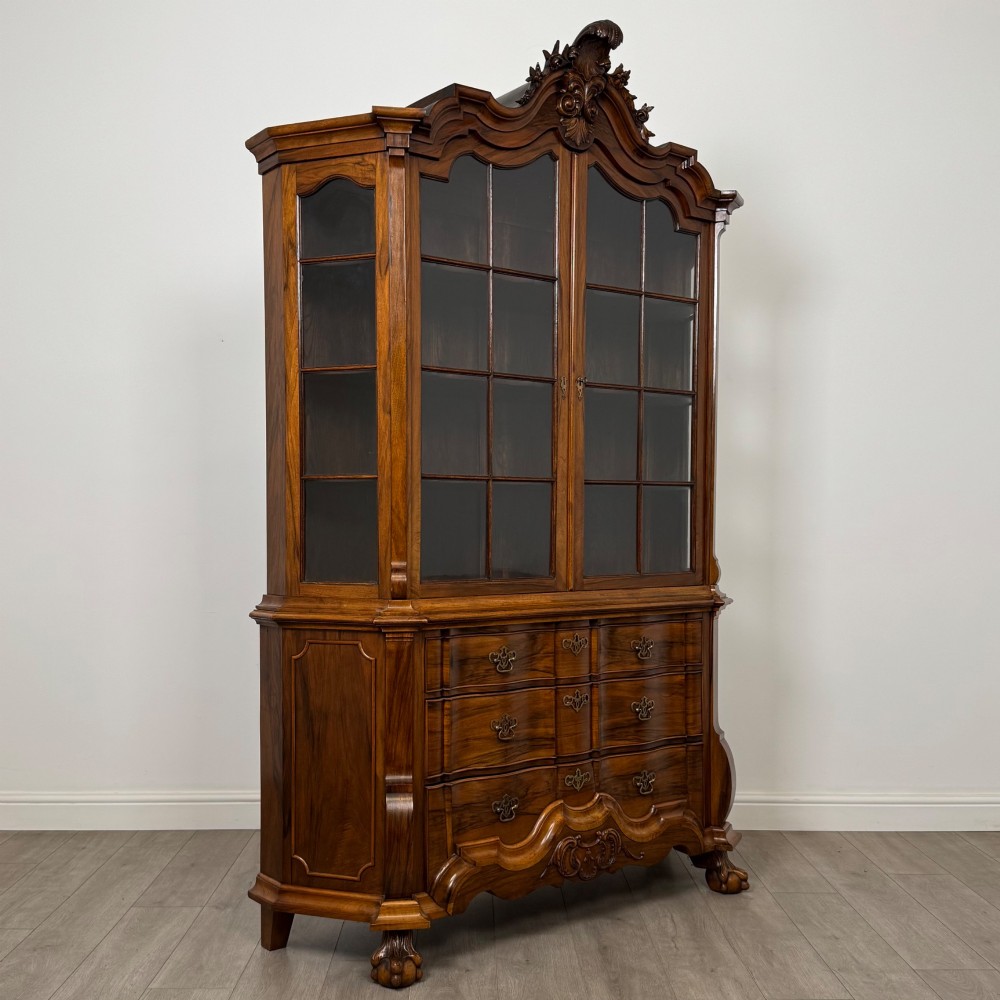 A Dutch walnut display cabinet featuring a carved bonnet-top pediment, multi-pane glazed doors, and a lower chest of drawers on carved claw-and-ball feet. View IX
