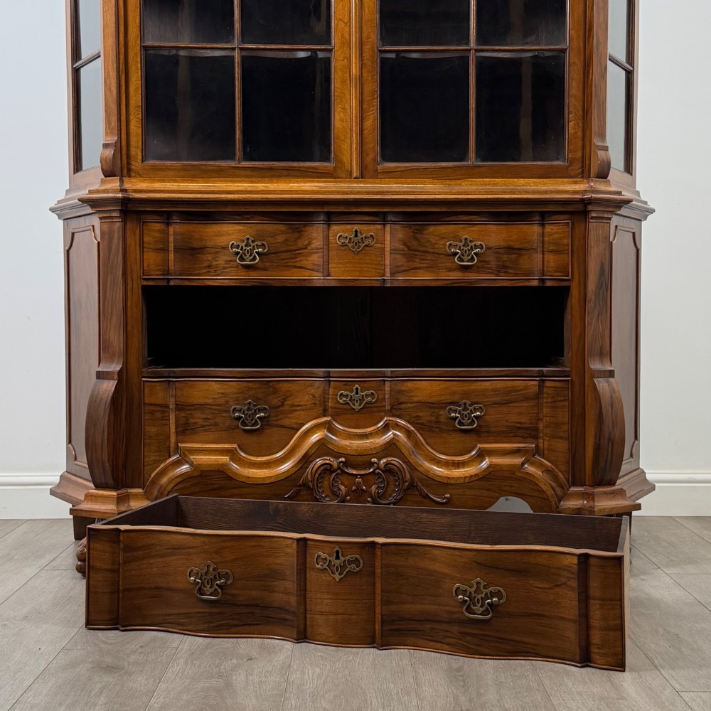 A Dutch walnut display cabinet featuring a carved bonnet-top pediment, multi-pane glazed doors, and a lower chest of drawers on carved claw-and-ball feet. View X