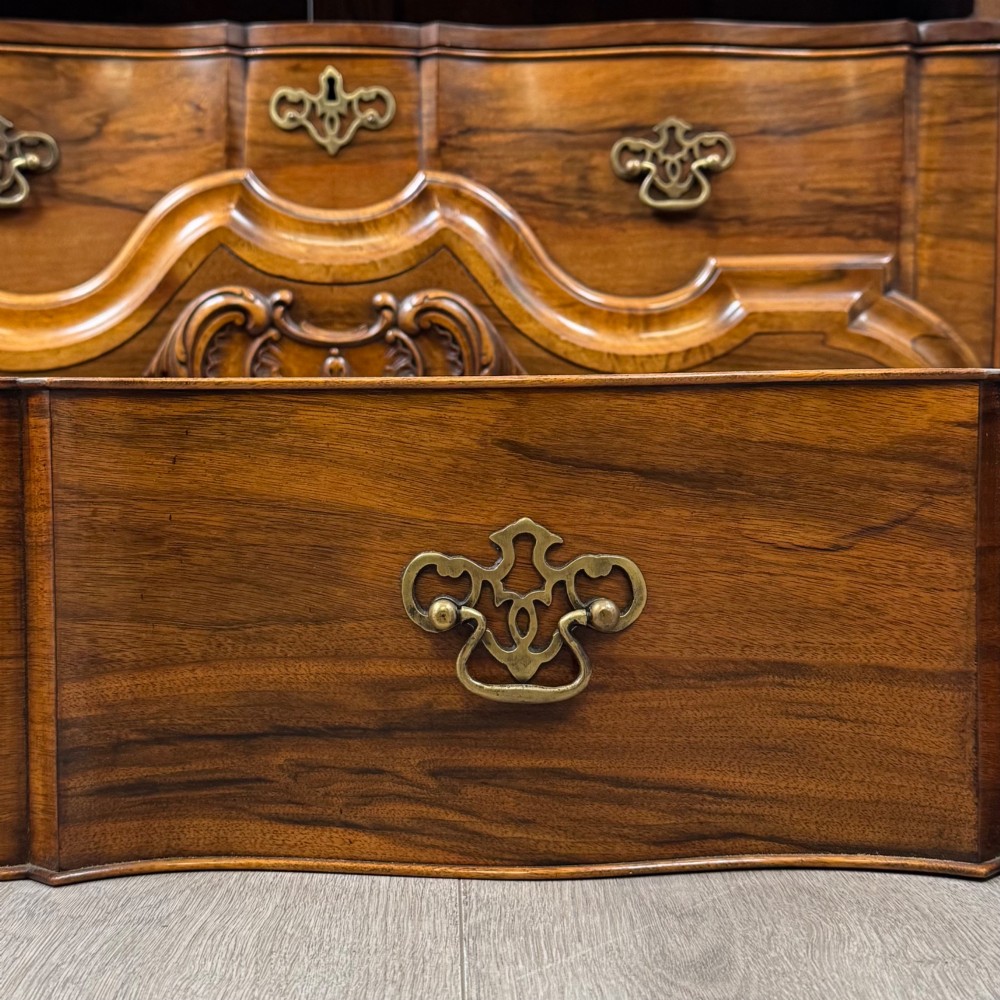 A Dutch walnut display cabinet featuring a carved bonnet-top pediment, multi-pane glazed doors, and a lower chest of drawers on carved claw-and-ball feet. View XI