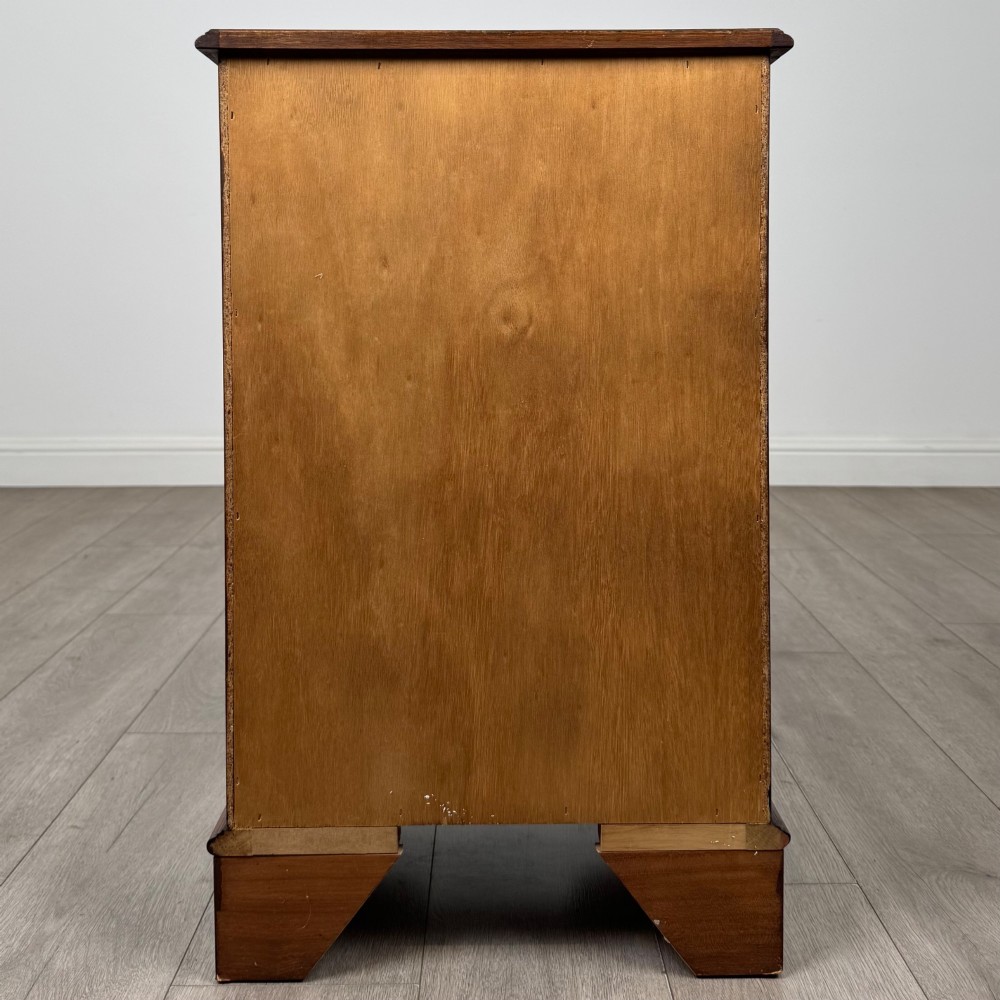 A small 20th-century serpentine chest of drawers with four drawers featuring burr walnut veneer, brass drop handles, and bracket feet. View V