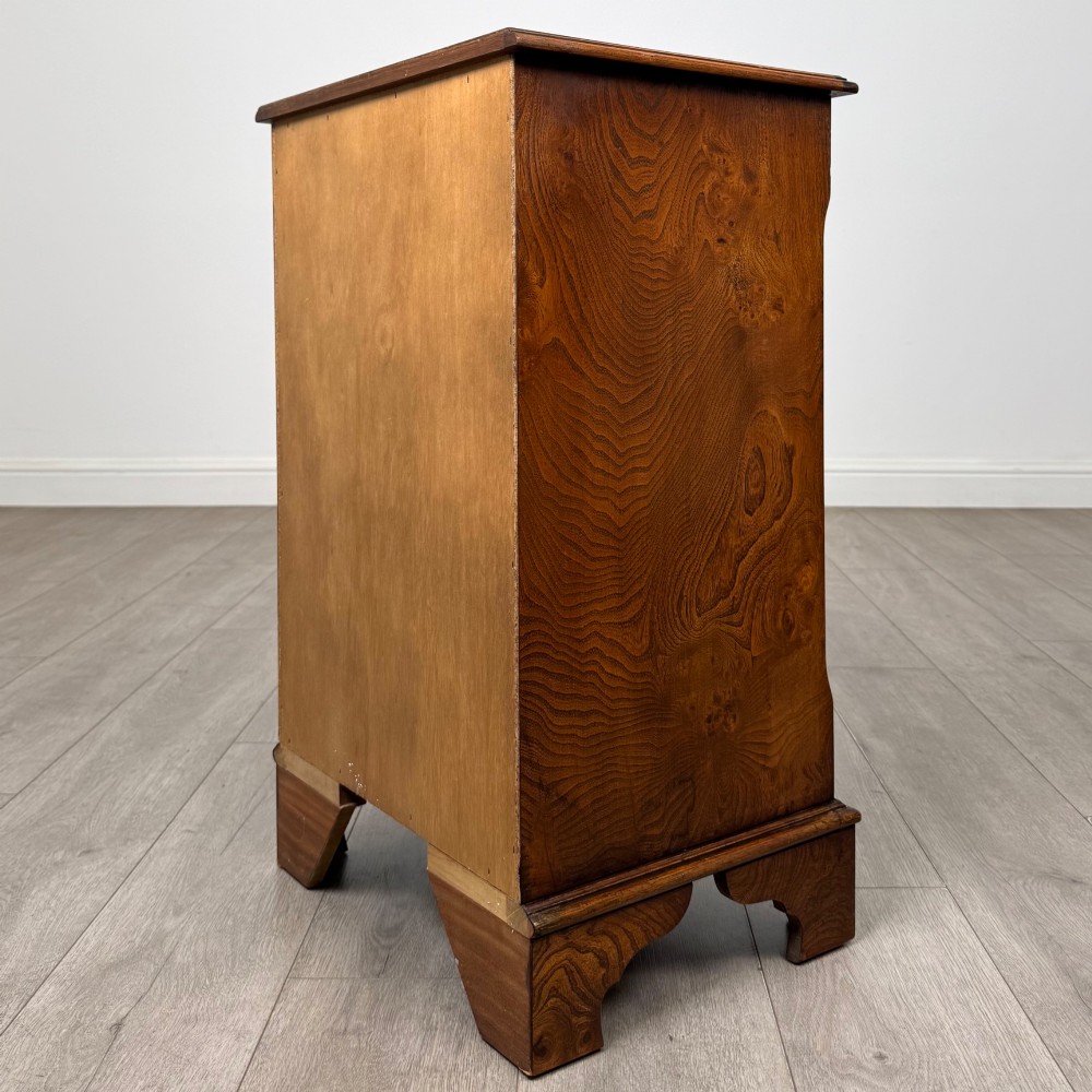 A small 20th-century serpentine chest of drawers with four drawers featuring burr walnut veneer, brass drop handles, and bracket feet. View VI