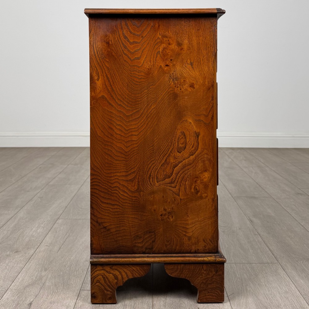 A small 20th-century serpentine chest of drawers with four drawers featuring burr walnut veneer, brass drop handles, and bracket feet. View VII