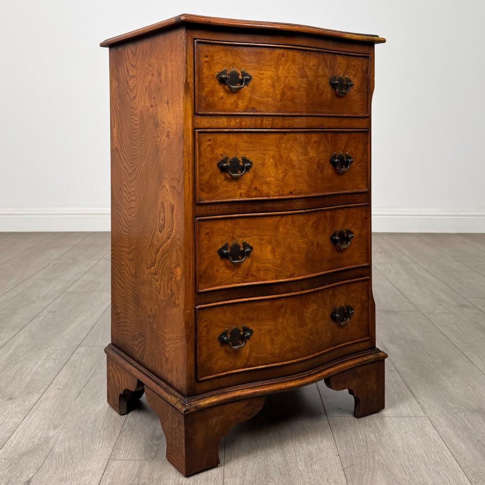 A small 20th-century serpentine chest of drawers with four drawers featuring burr walnut veneer, brass drop handles, and bracket feet. View VIII