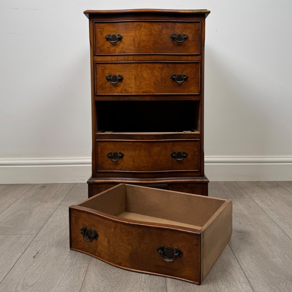 A small 20th-century serpentine chest of drawers with four drawers featuring burr walnut veneer, brass drop handles, and bracket feet. View X