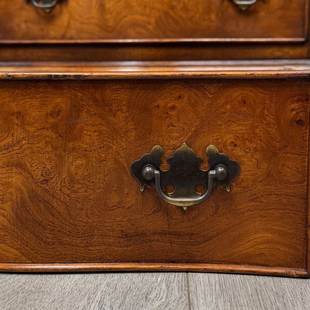 A small 20th-century serpentine chest of drawers with four drawers featuring burr walnut veneer, brass drop handles, and bracket feet. View XI