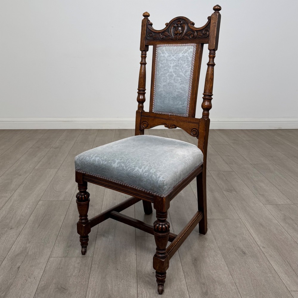 A set of four 19th-century Victorian dark oak dining chairs featuring carved crest rails, turned legs, and light blue patterned fabric upholstery on the seats and backrests. View II