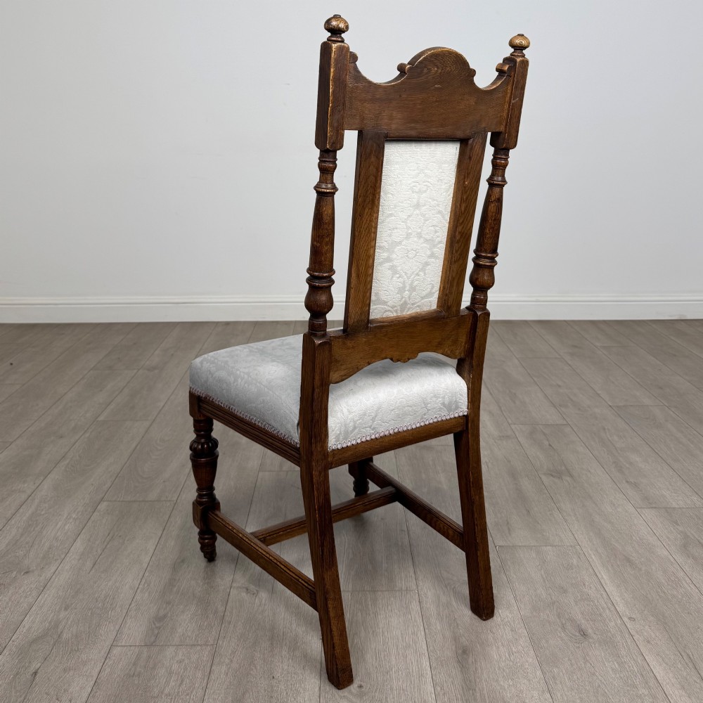 A set of four 19th-century Victorian dark oak dining chairs featuring carved crest rails, turned legs, and light blue patterned fabric upholstery on the seats and backrests. View III