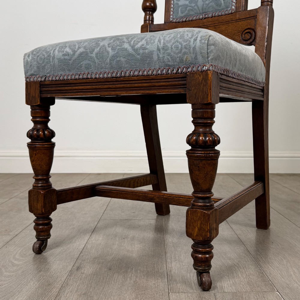 A set of four 19th-century Victorian dark oak dining chairs featuring carved crest rails, turned legs, and light blue patterned fabric upholstery on the seats and backrests. View V
