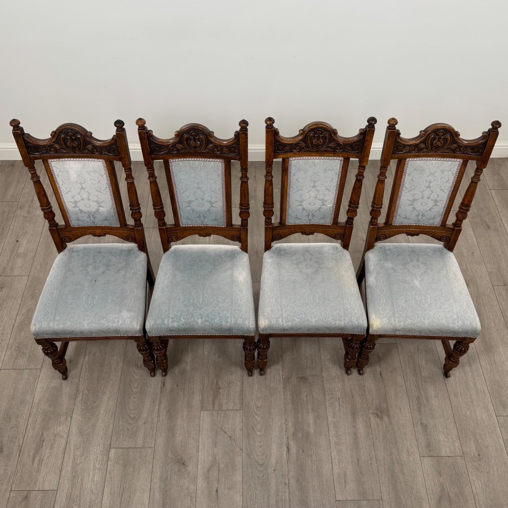 A set of four 19th-century Victorian dark oak dining chairs featuring carved crest rails, turned legs, and light blue patterned fabric upholstery on the seats and backrests. View VII