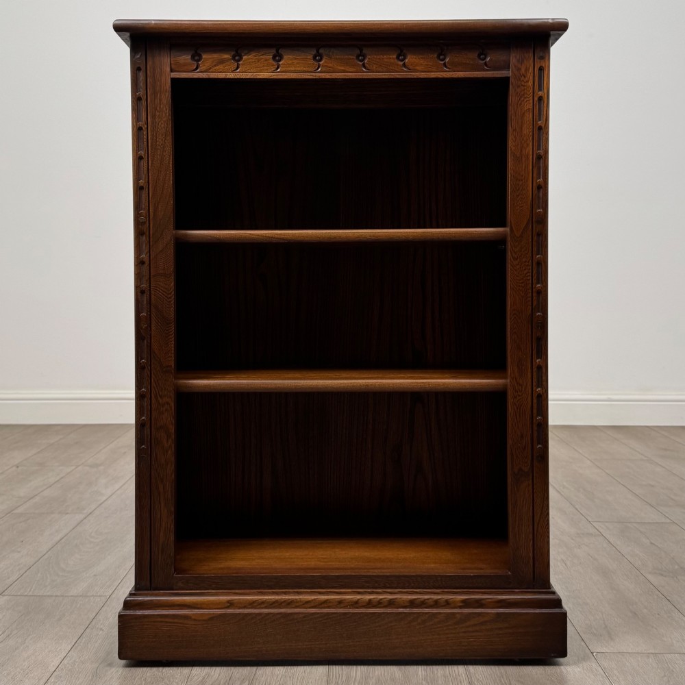 A small vintage dark oak bookcase featuring three open shelves, decorative carved detailing along the frieze and side uprights, and a solid plinth base. View II