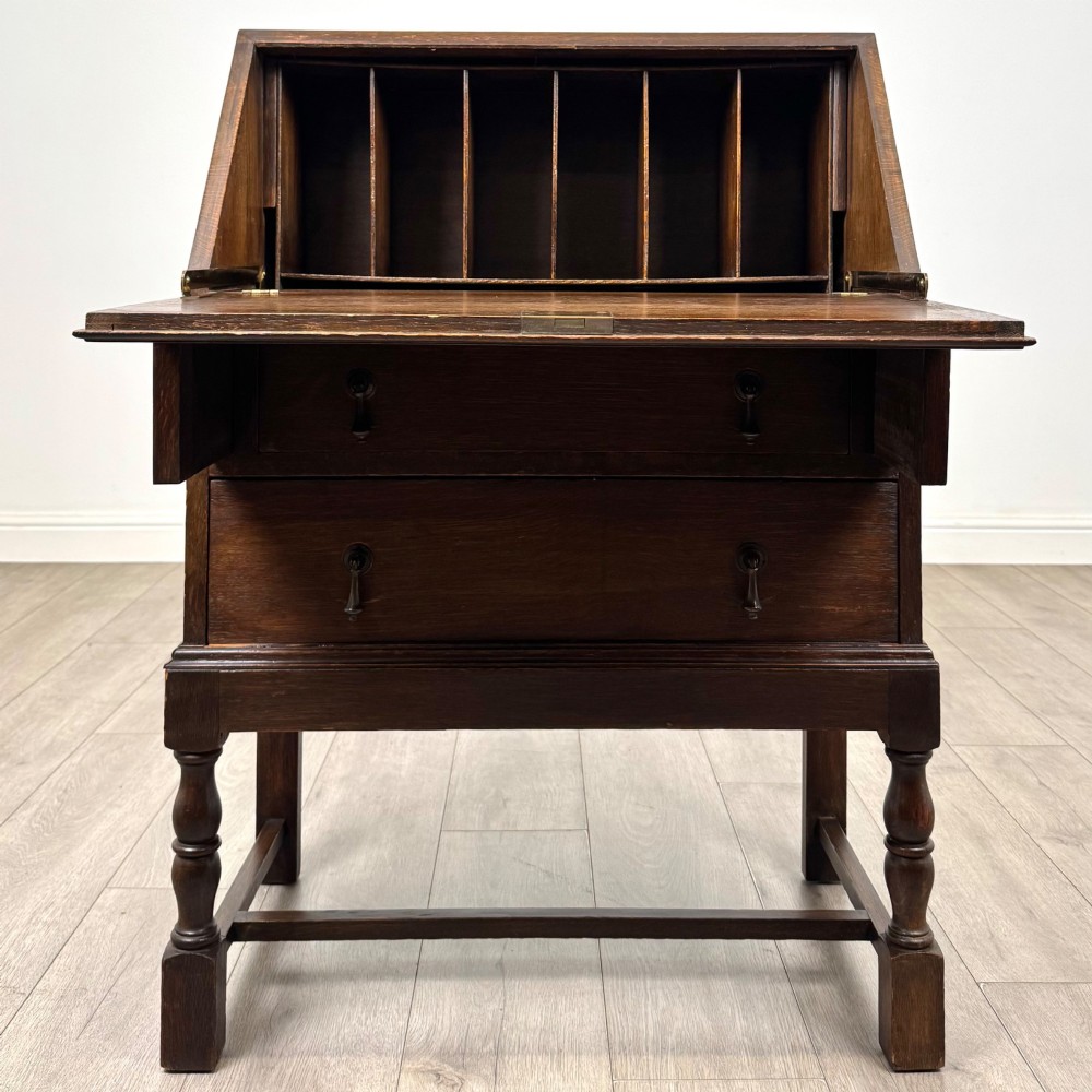 An Edwardian dark oak writing bureau featuring a sloped drop-down lid, two lower drawers with teardrop handles, and turned legs connected by stretchers. View II