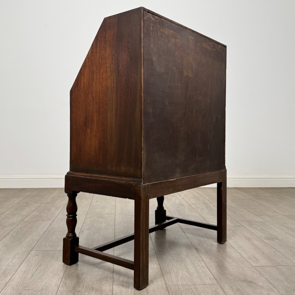 An Edwardian dark oak writing bureau featuring a sloped drop-down lid, two lower drawers with teardrop handles, and turned legs connected by stretchers. View V