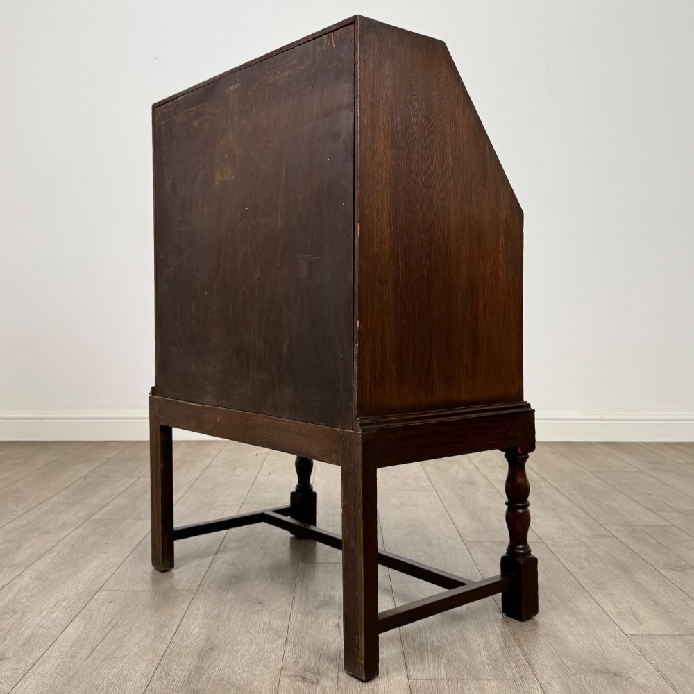 An Edwardian dark oak writing bureau featuring a sloped drop-down lid, two lower drawers with teardrop handles, and turned legs connected by stretchers. View VII