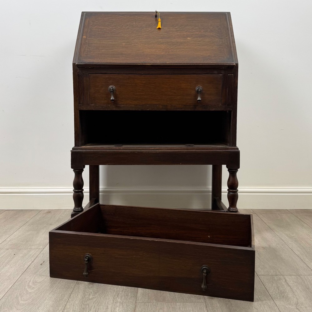 An Edwardian dark oak writing bureau featuring a sloped drop-down lid, two lower drawers with teardrop handles, and turned legs connected by stretchers. View XII