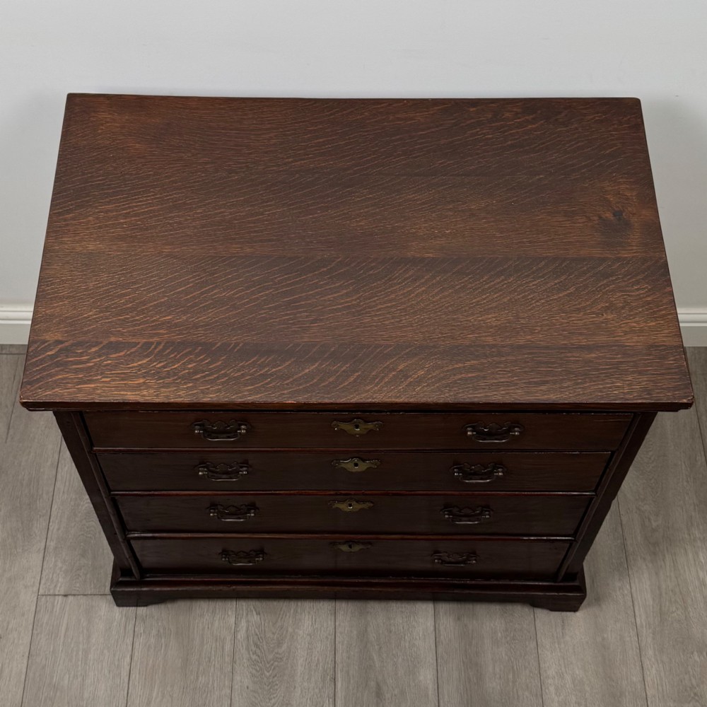 An 18th-century dark oak Georgian chest of drawers featuring four graduated drawers with brass handles and keyhole escutcheons. View IX