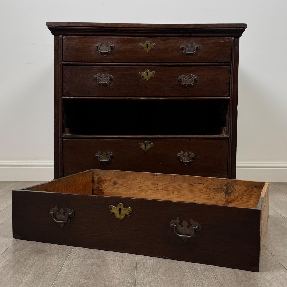 An 18th-century dark oak Georgian chest of drawers featuring four graduated drawers with brass handles and keyhole escutcheons. View X