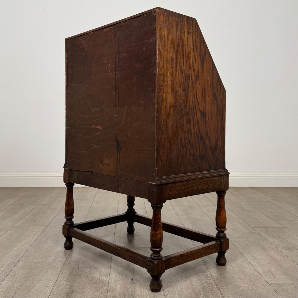 An Edwardian golden oak writing bureau featuring a slant-front writing flap above two drawers with brass teardrop handles, supported on turned legs with a perimeter stretcher. View VII