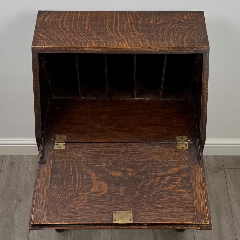 An Edwardian golden oak writing bureau featuring a slant-front writing flap above two drawers with brass teardrop handles, supported on turned legs with a perimeter stretcher. View XI
