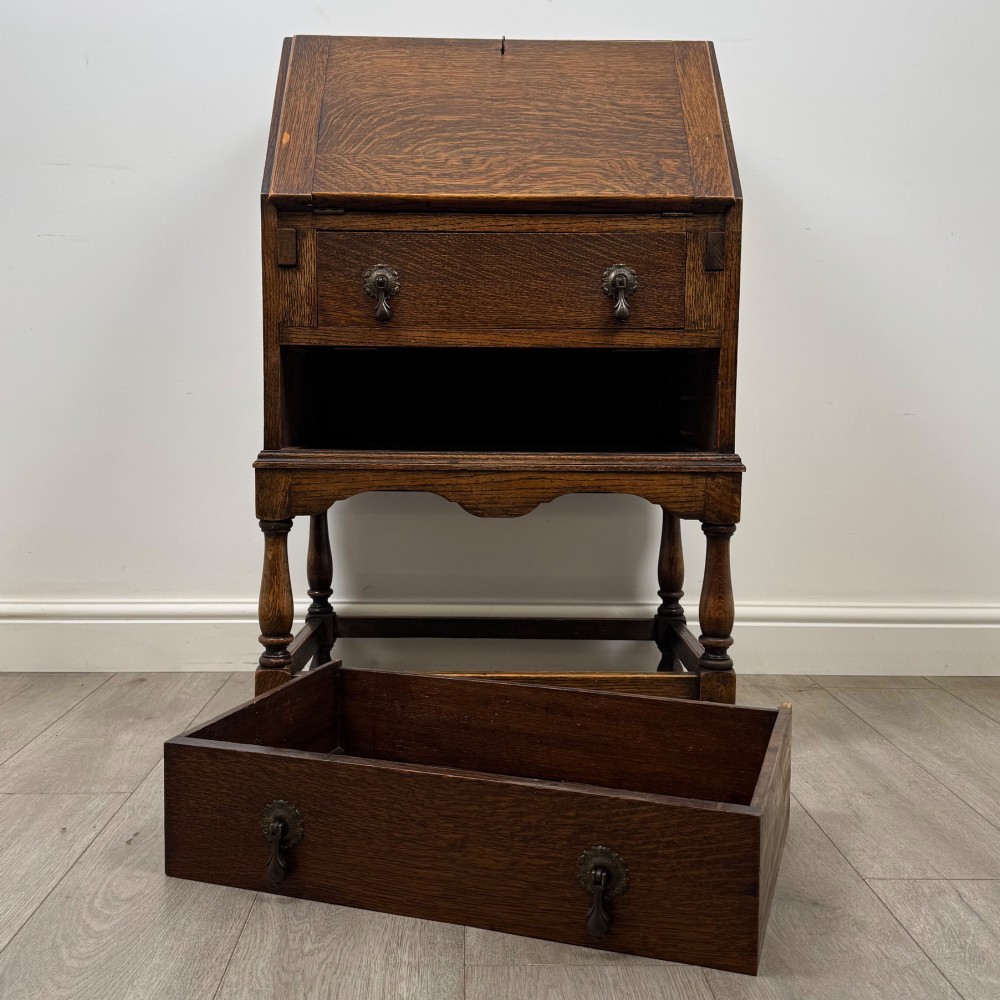 An Edwardian golden oak writing bureau featuring a slant-front writing flap above two drawers with brass teardrop handles, supported on turned legs with a perimeter stretcher. View XII