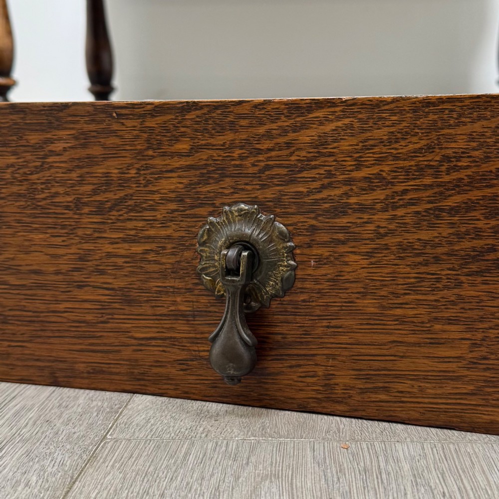 An Edwardian golden oak writing bureau featuring a slant-front writing flap above two drawers with brass teardrop handles, supported on turned legs with a perimeter stretcher. View XIII