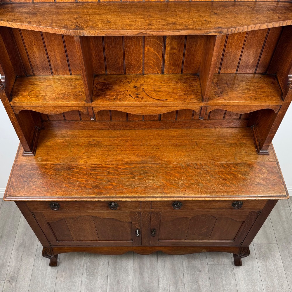 A 20th-century golden oak Welsh dresser featuring a three-tiered open shelf top section over a two-door, two-drawer base with cabriole legs. View X
