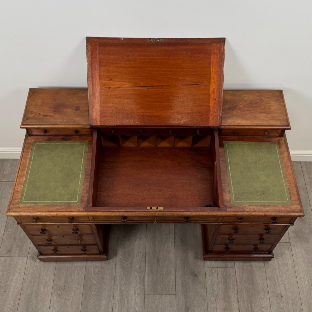 A 19th-century Victorian mahogany Dickens desk featuring a sloped green leather writing top, a raised rear superstructure, and twin pedestals fitted with turned knobs. View X