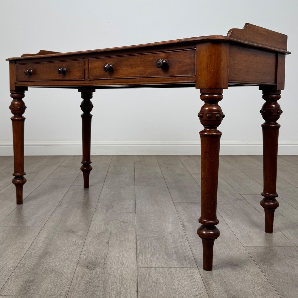 A 19th-century mahogany writing table featuring two frieze drawers with wooden turned handles, standing on four turned legs. View II