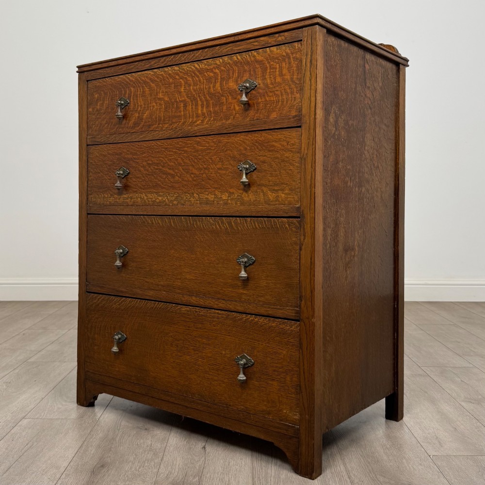 Front view of an early 20th-century warm brown oak chest featuring four wide drawers with ornamental brass drop handles. View II