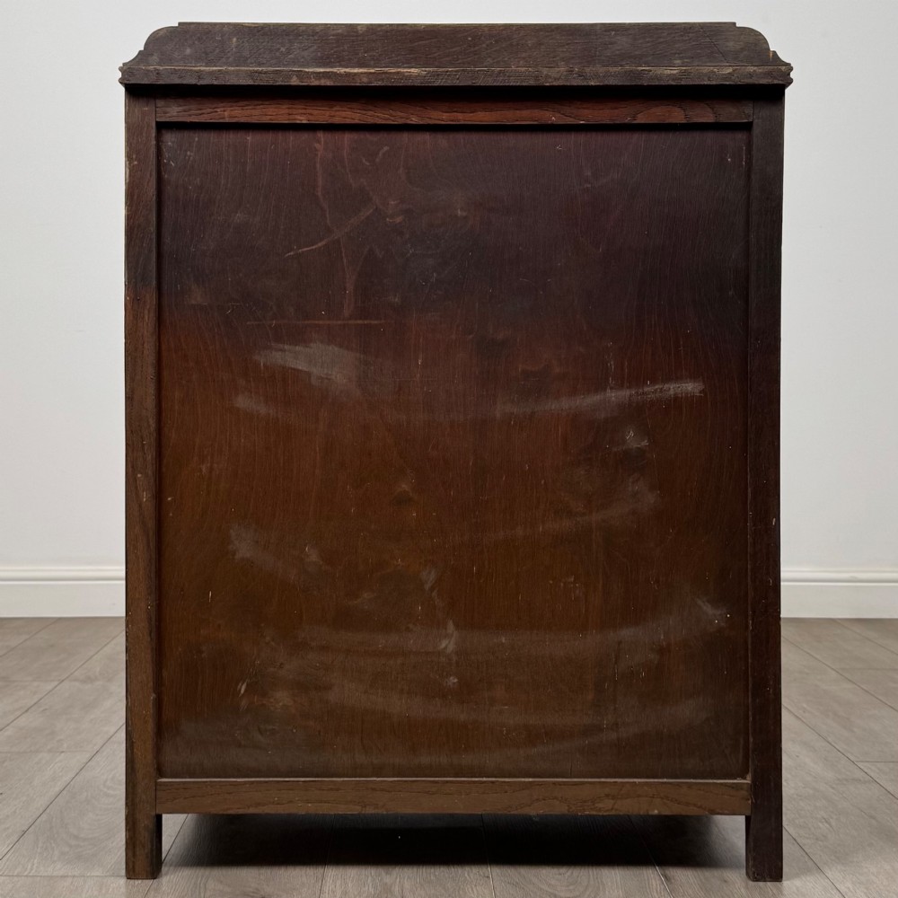 Front view of an early 20th-century warm brown oak chest featuring four wide drawers with ornamental brass drop handles. View V