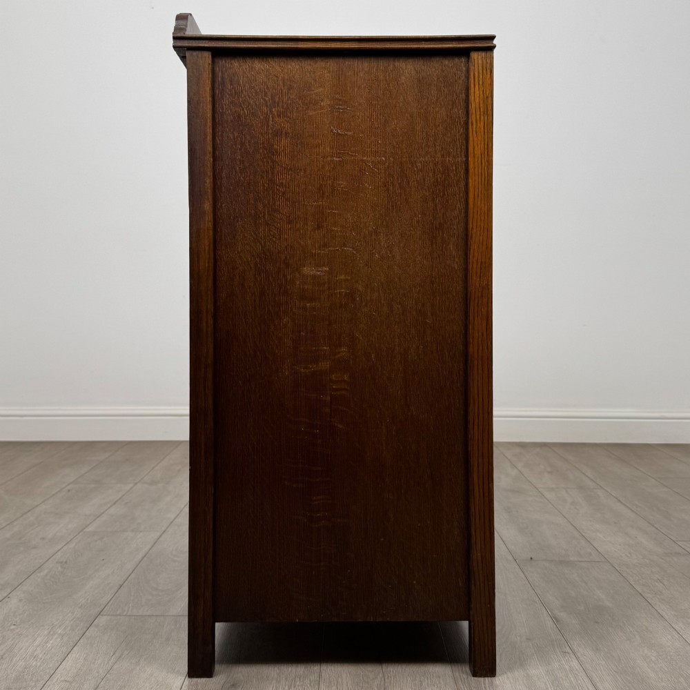 Front view of an early 20th-century warm brown oak chest featuring four wide drawers with ornamental brass drop handles. View VII