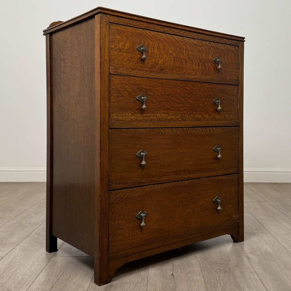 Front view of an early 20th-century warm brown oak chest featuring four wide drawers with ornamental brass drop handles. View VIII