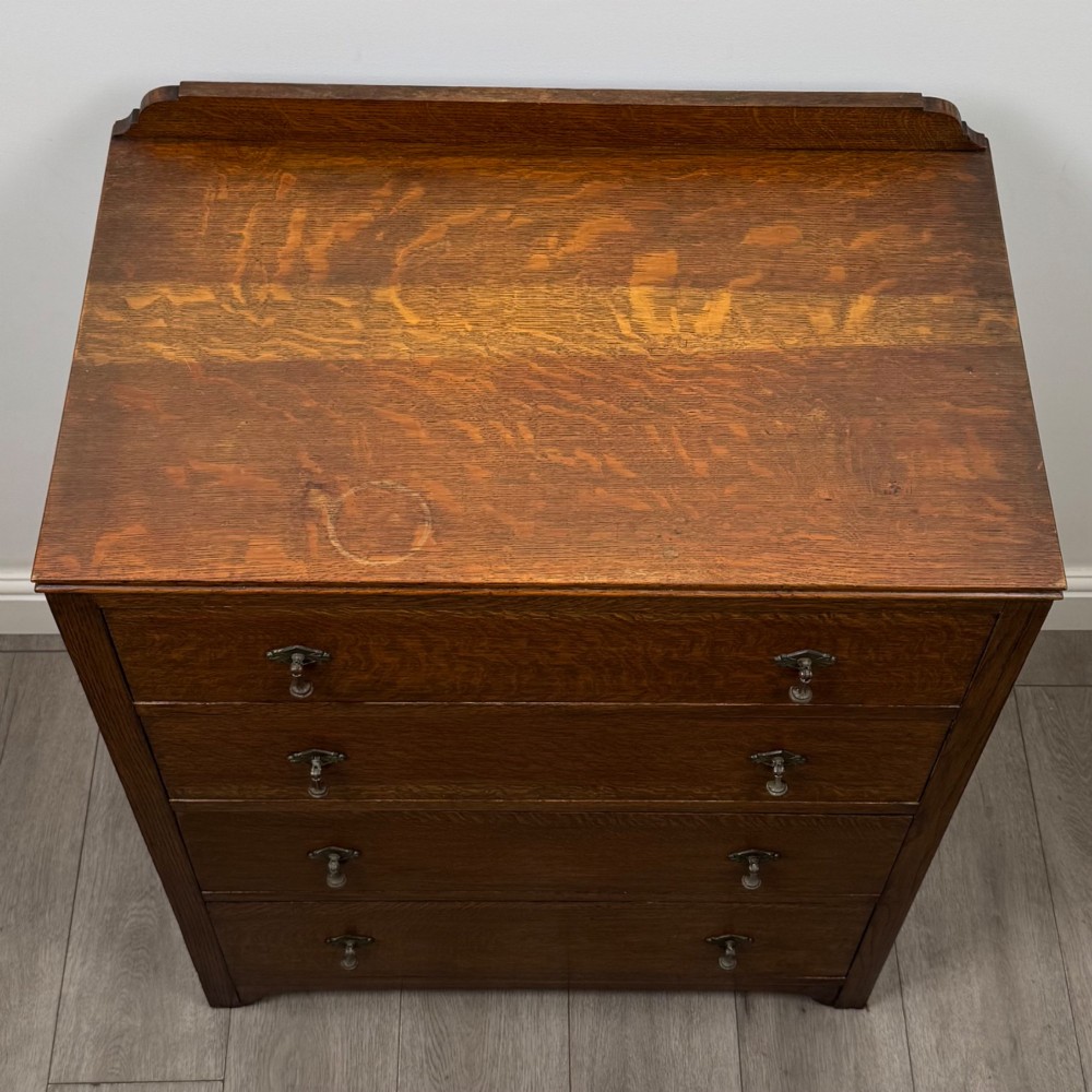 Front view of an early 20th-century warm brown oak chest featuring four wide drawers with ornamental brass drop handles. View IX