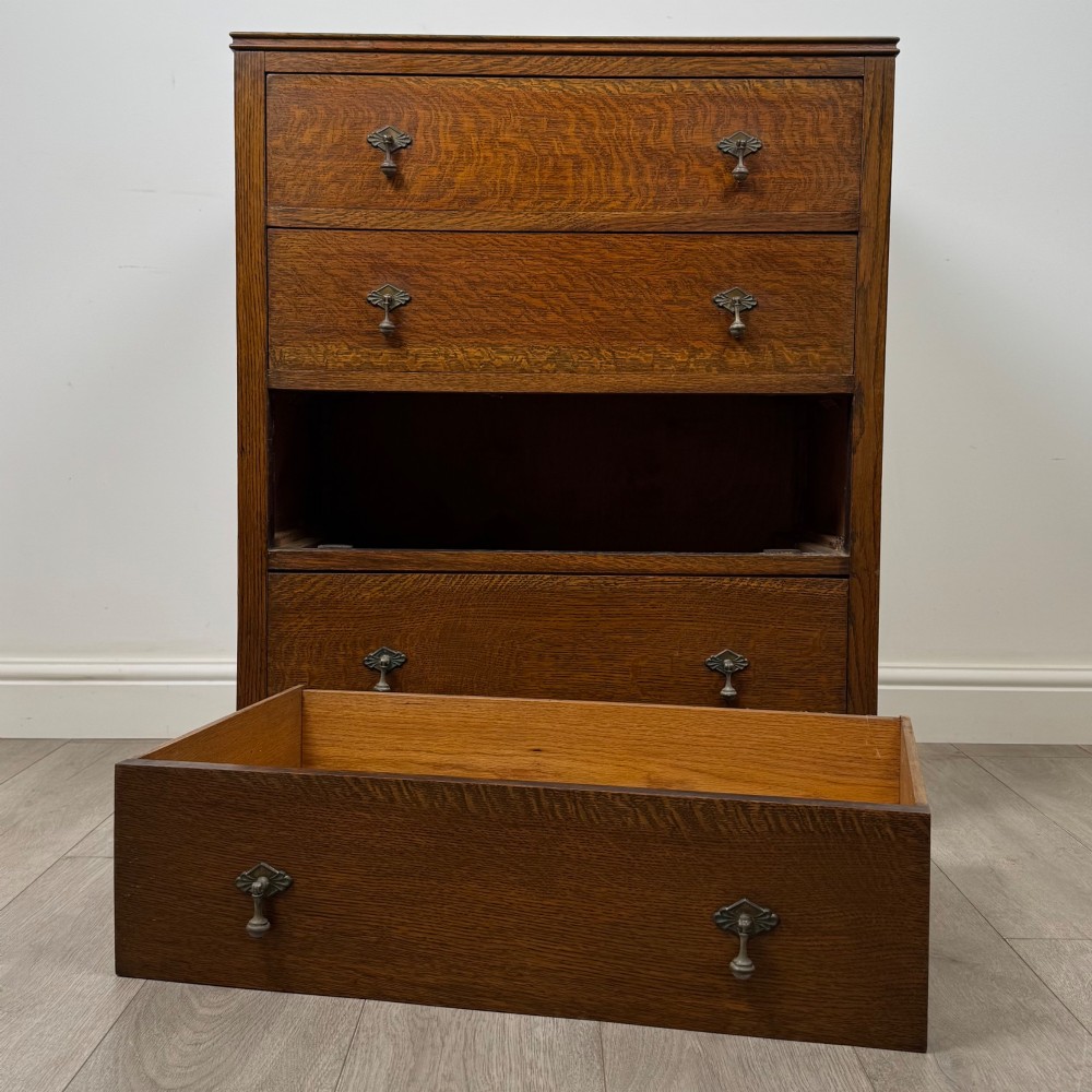 Front view of an early 20th-century warm brown oak chest featuring four wide drawers with ornamental brass drop handles. View X