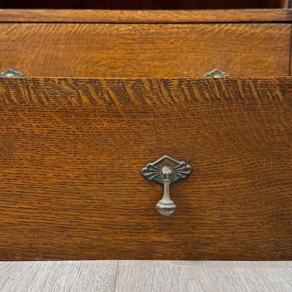 Front view of an early 20th-century warm brown oak chest featuring four wide drawers with ornamental brass drop handles. View XI