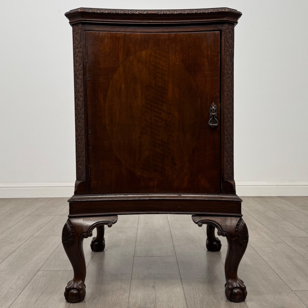A dark mahogany Chippendale style cupboard featuring a single door with an oval flame mahogany panel, carved borders, and cabriole legs with ball-and-claw feet.