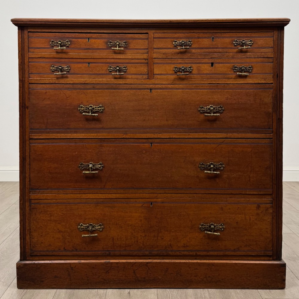 An antique walnut chest of drawers featuring decorative brass handles, reeded top drawer fronts, and a solid plinth base.