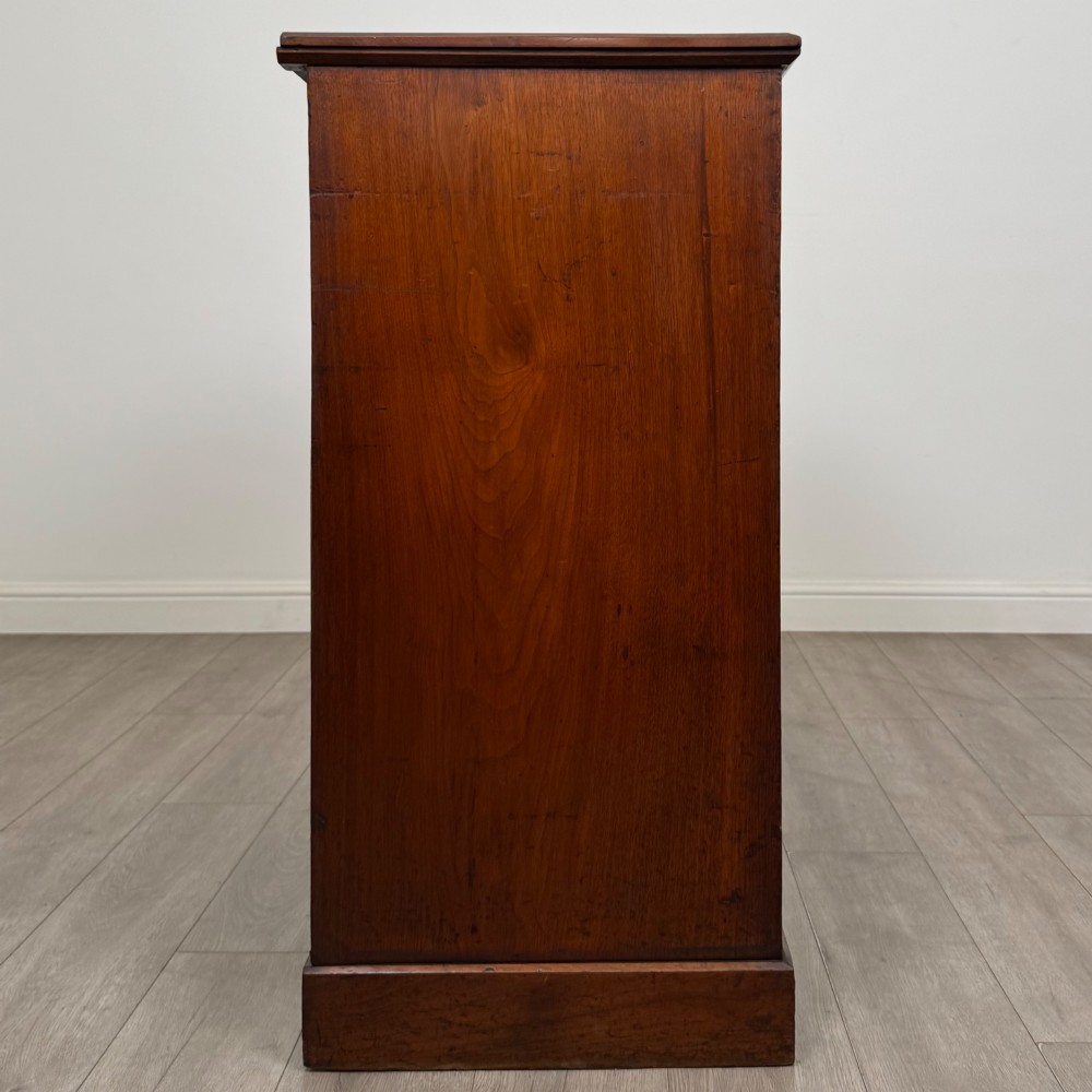 An antique walnut chest of drawers featuring decorative brass handles, reeded top drawer fronts, and a solid plinth base. View VII