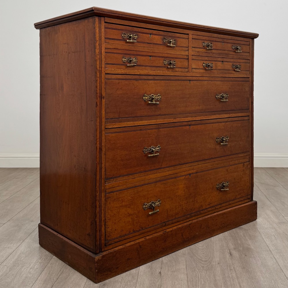 An antique walnut chest of drawers featuring decorative brass handles, reeded top drawer fronts, and a solid plinth base. View VIII